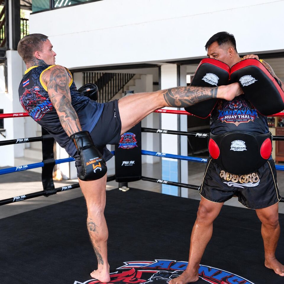 A student lands a high kick on the pads held by a Kiat Payak trainer in the ring