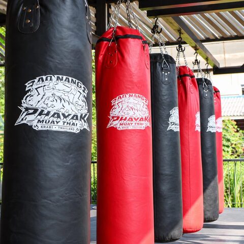A row of red and black heavy bags under the roof of the open-air gym